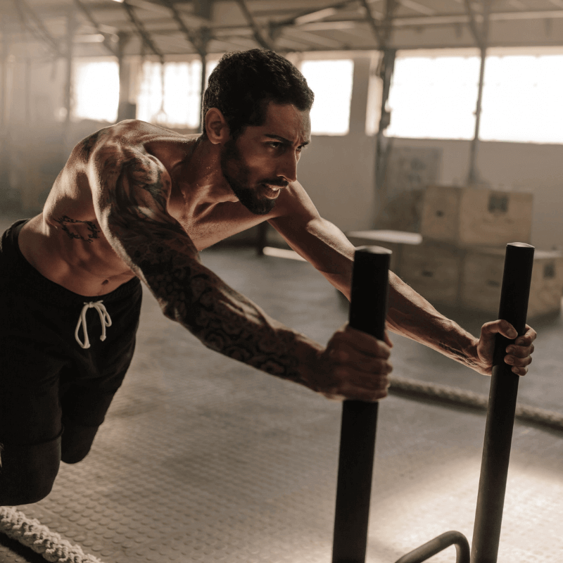 A muscular man pushing a sled in a gym, embodying the power of discipline over motivation in fitness.